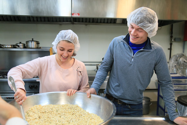 Two smiling students mixing ingredients in a large metal bowl