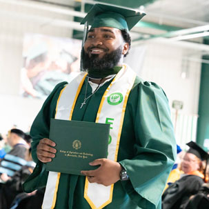 Student at commencement, smiling and holding their diploma