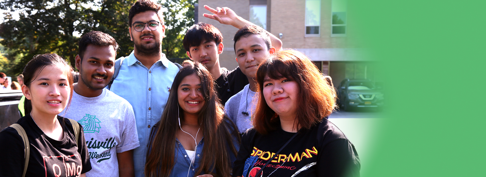 Diverse group of students smiling in front of a building and trees.