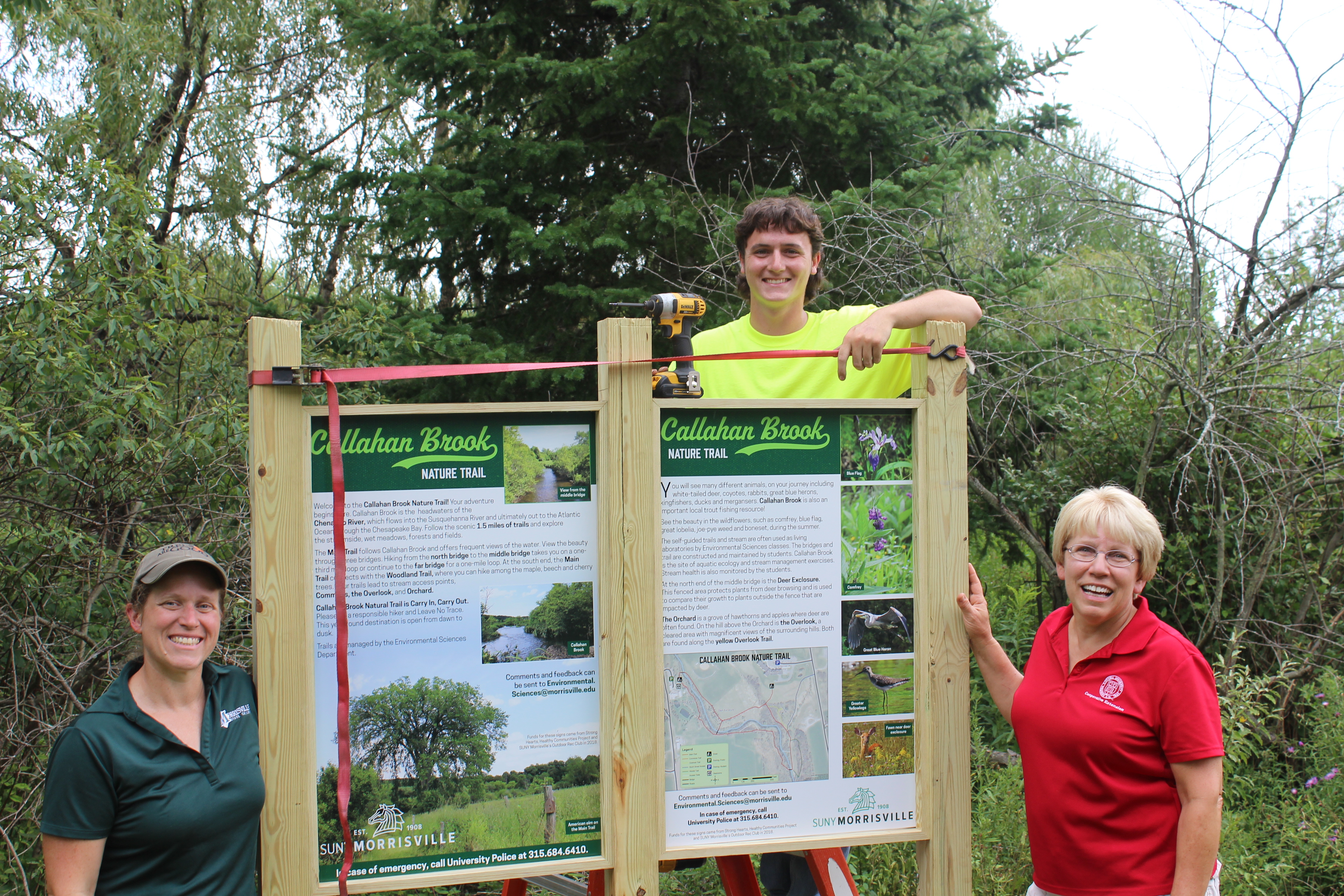 SUNY Morrisville assistant professor of environmental sciences Rebecca Hargrave (left), student and summer forestry aide Andrew Gardner (center) and Cornell Cooperative Extension educator Debbie SeGuin (right) help install the new entrance kiosk at Callahan Brook Nature Trail.