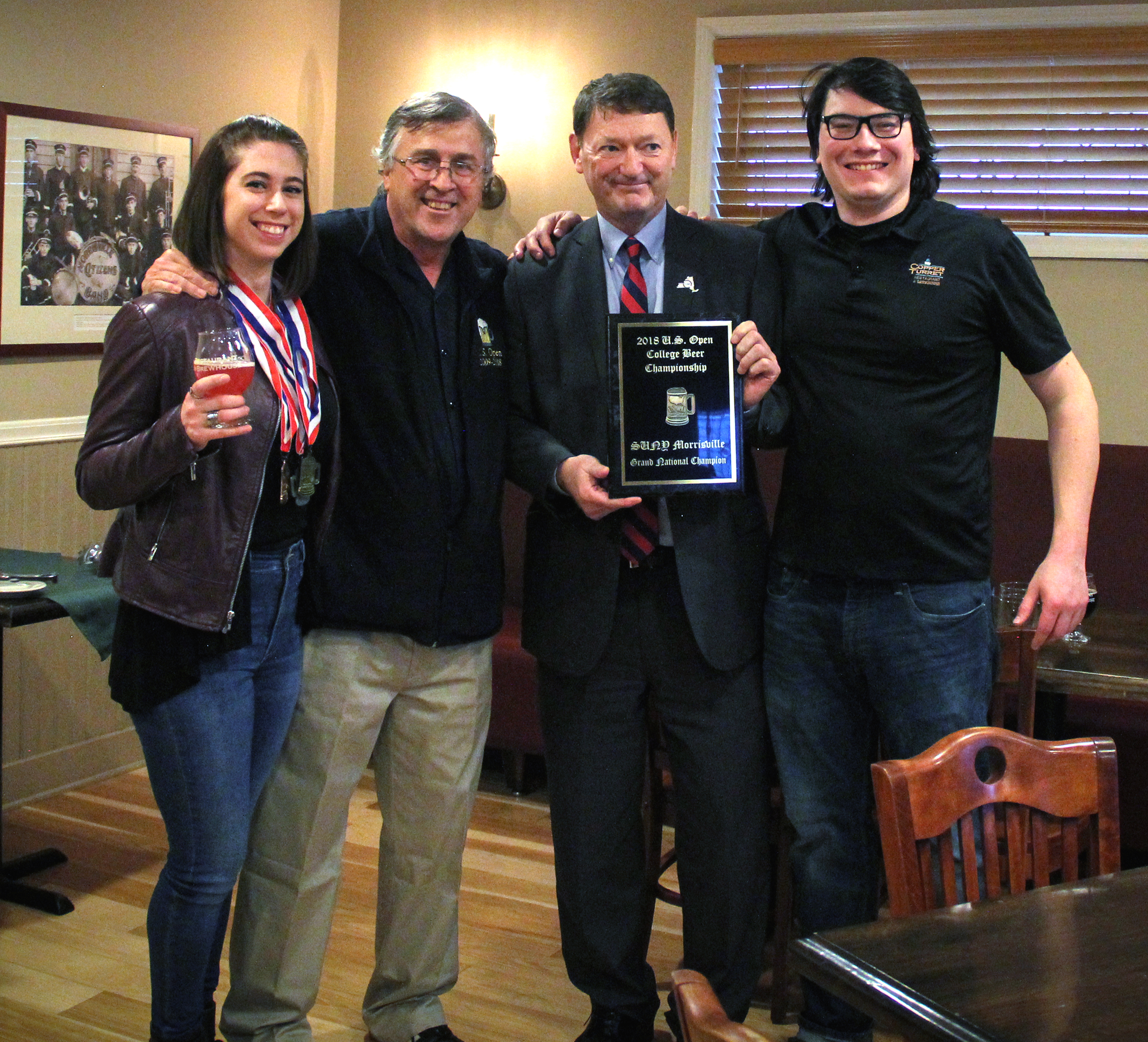 SUNY Morrisville President David Rogers (second from right), head brewer Micheal Coons (far right) and student Mary Cosenza (far left) were presented with a championship plaque by U.S. Open Beer Championships Director Dow Scoggins. Morrisville was named Grand National Champion of this year's competition (Photo credit Sarah Marcellus, MAC Associate Graphic Designer).