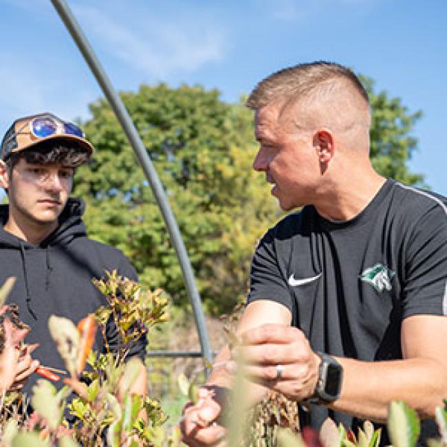 Adam Olinski works with a horticulture student in the greenhouse.