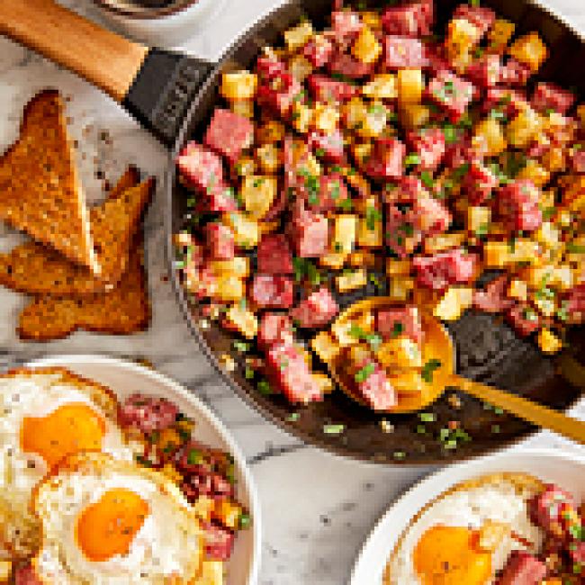 Skillet with corned beef hash and potatoes with a side of two over-easy eggs and toast