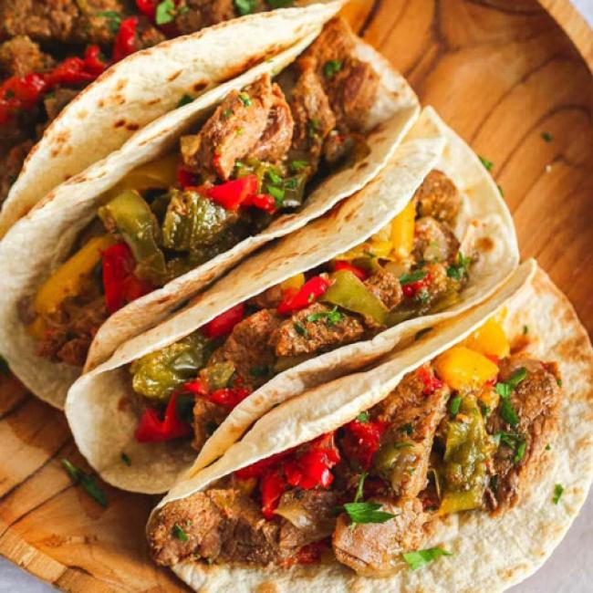 three soft tortillas holding fajita meat and vegetables