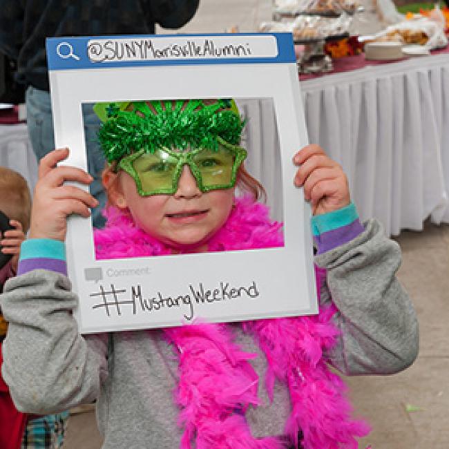 Decorated child holds up a #MustangWeekend photo frame