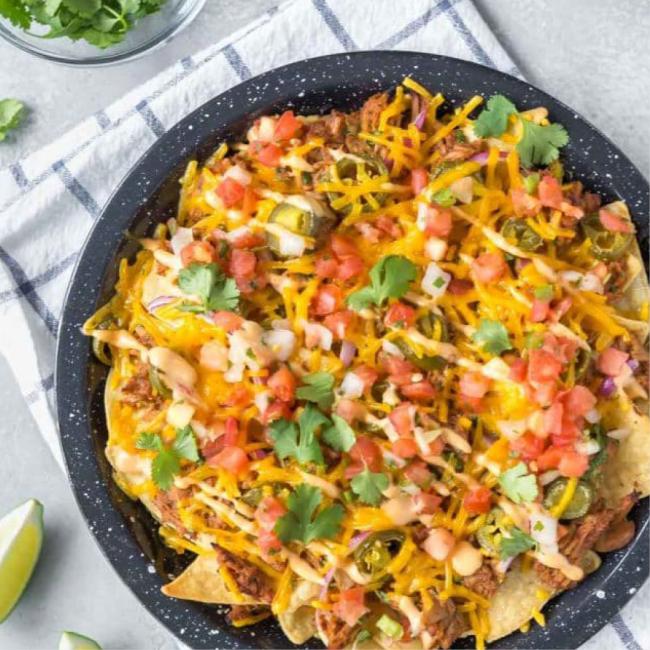 Bowl of loaded nachos with cheese, meat, tomatoes and fresh cilantro