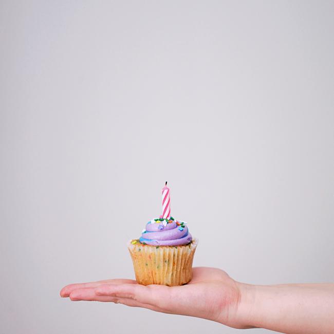 Hand holding cupcake with candle on it