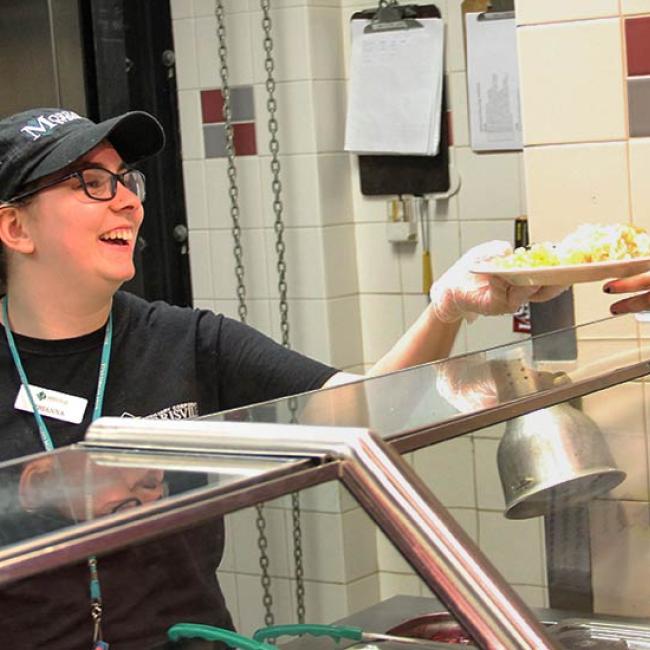A work-study student serves up a meal at Seneca Dining Hall.