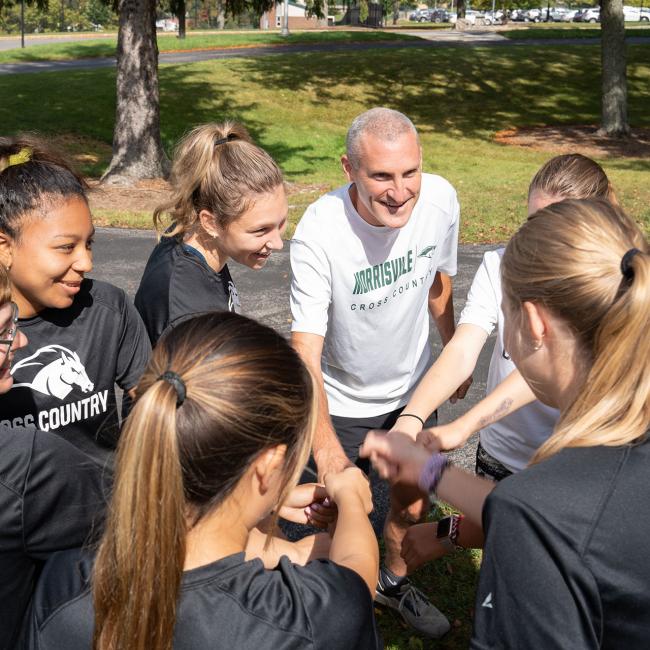 Coach Derek Powers forms a huddle with members of the women’s cross-country team.