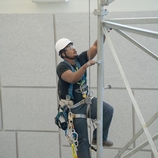 A renewable energy student climbs a tower in the college's ACET Center