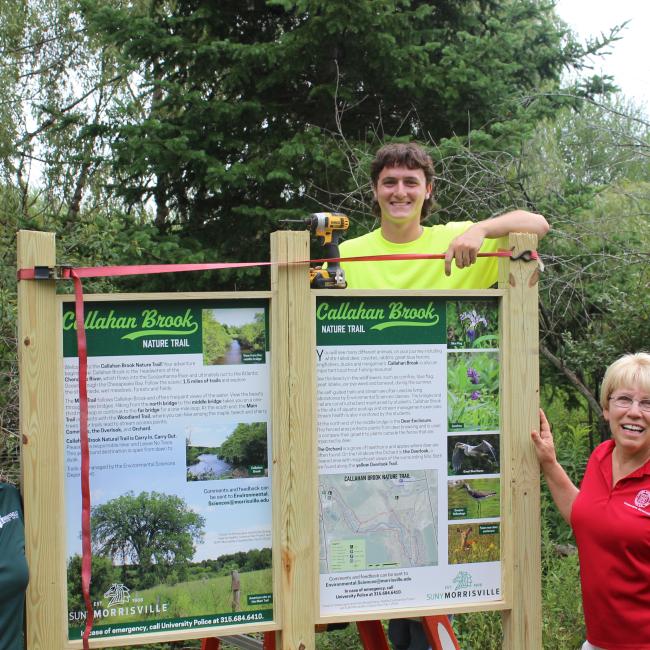 SUNY Morrisville assistant professor of environmental sciences Rebecca Hargrave (left), student and summer forestry aide Andrew Gardner (center) and Cornell Cooperative Extension educator Debbie SeGuin (right) help install the new entrance kiosk at Callahan Brook Nature Trail.