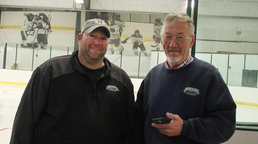 Two people standing in front of an ice rink and smiling