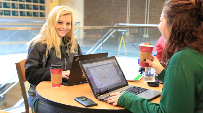 Two students sitting at a table. Student is smiling at the camera.