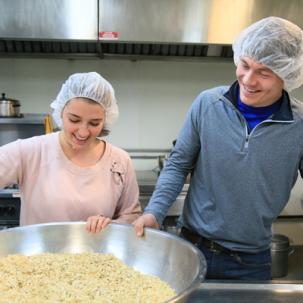 Two smiling students mixing ingredients in a large metal bowl