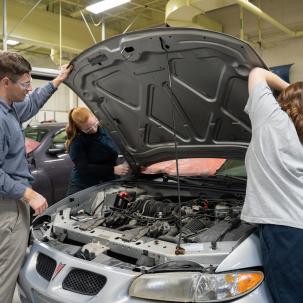 Auto students and their instructor remove the hood of a car